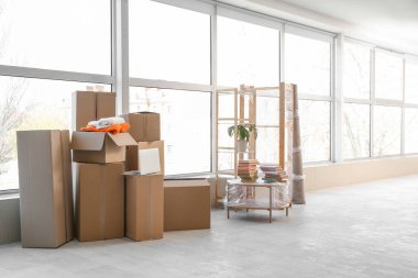 Taşındığı gün şık bir odada cam kenarında rulo halı, sehpa ve karton kutular.