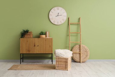 Çekmeceler, ev bitkileri ve yeşil duvardaki saat.