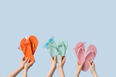 Mavi arka planda güneş gözlüklü üç çift parmak arası terlik tutan eller.