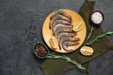 Koyu arkaplanda taze çiğ karides, limon ve biberiye tabağı.