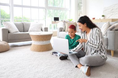Annesi evde dizüstü bilgisayar kullanan küçük bir Afro-Amerikalı çocuk.