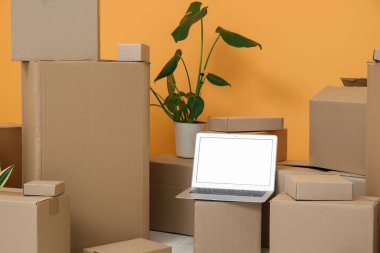 Boş dizüstü bilgisayar, taşınan kutular ve turuncu duvarın yanına yerleştirme