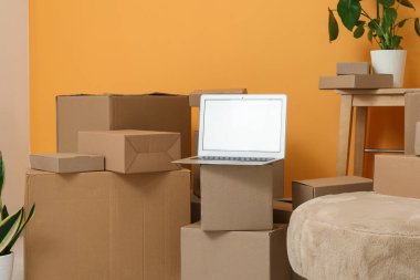 Turuncu duvarın yanındaki kutuları taşıyan boş dizüstü bilgisayar.