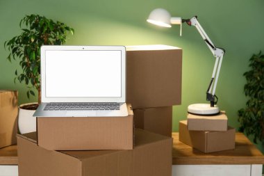 Parlayan lamba ve yeşil duvarın yanındaki kutuları taşıyan boş bir laptop.
