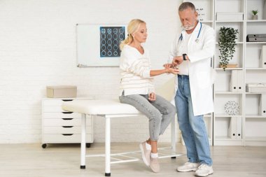 Akıllı erkek doktor klinikte olgun bir kadının nabzını kontrol ediyor.