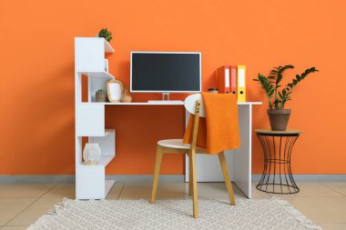 Turuncu duvarın yanında modern bilgisayarla rahat çalışma alanı