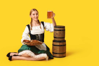 Güzel mutlu Ekim Festivali garsonu bira fıçıları ve sarı arka planda oturan geleneksel yemek tabağıyla