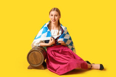 Sarı arka planda oturan bira fıçısı ve Bavyera bayrağıyla güzel mutlu bir Ekim Festivali garsonu.