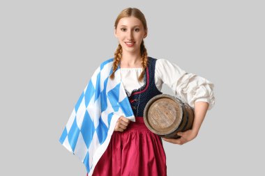 Gri arka planda Bavyera bayrağı ve bira fıçısıyla güzel mutlu bir Ekim Festivali garsonu.