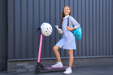Dışarıda elektrikli scooterlı ve kasklı tatlı bir kız öğrenci.