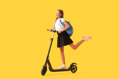 Sarı arka planda elektrikli scooter kullanan tatlı bir kız öğrenci.