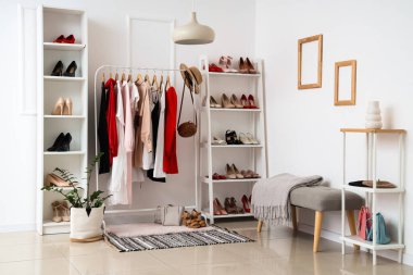 Kıyafet rafları ve gardıroptaki beyaz duvarın yanında farklı kadın ayakkabıları olan raflar.