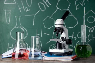 Modern mikroskop ve mataralar ahşap masada, kimyasal formüllerle birlikte.