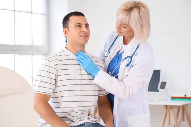 Kadın endokrinolojist klinikteki adamın tiroit bezini inceliyor.