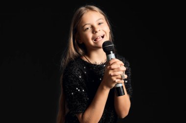 Mikrofonlu küçük kız siyah arka planda şarkı söylüyor.