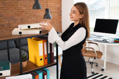 Ofisteki raflarda doküman klasörleri olan genç iş kadını.