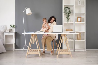 Çalışan anne evde bebeğiyle cep telefonuyla konuşuyor.