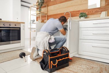 Erkek muslukçu mutfakta lavaboyu tamir ediyor.