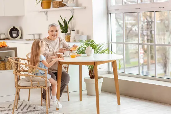 Mutfaktaki masada büyükannesiyle waffle yiyen tatlı küçük kız.