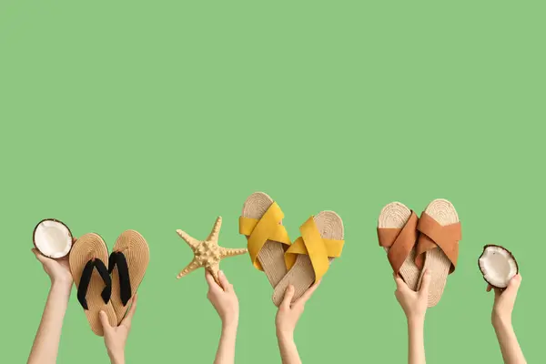 stock image Hands holding three pairs of flip flops with starfish and coconut on green background