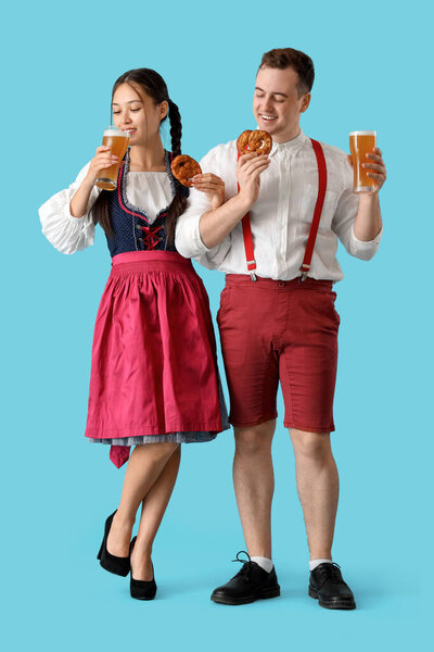Молодая счастливая пара в традиционной немецкой одежде с крендельками и бокалами пива на синем фоне