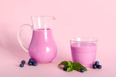 Pembe arka planda naneli bir bardak ve bir sürahi taze yaban mersini smoothie.