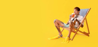 Genç dövmeli adam güverte sandalyesinde dinlenirken bira içiyor sarı arka planda mesaj için yer var.