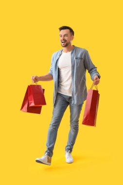 Sarı arka planda alışveriş torbaları olan mutlu genç adam.