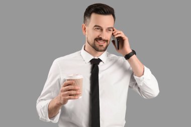 Gri arka planda cep telefonuyla konuşan kahve fincanı olan yakışıklı iş adamı.