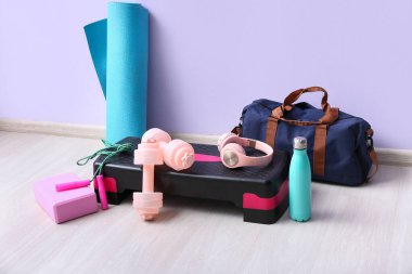 Spor aletleri ve kulaklıklar spor salonunda eflatun duvarın yanında.