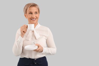 Gri arka planda kahve içen olgun bir iş kadını.