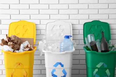 Geri dönüşüm sembollü çöp kutuları ve beyaz tuğla duvarın yanındaki farklı çöpler.