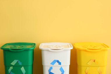 Sarı duvarın yanında geri dönüşüm sembolü olan farklı çöp bidonları