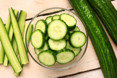 Hafif ahşap arka planda taze kesilmiş salatalıklı kase, yakın plan.