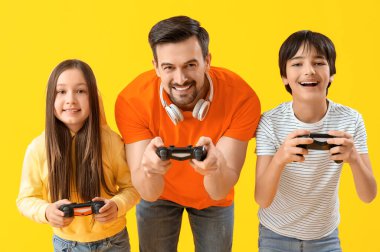 Baba ve küçük çocukları sarı arka planda video oyunu oynuyorlar.
