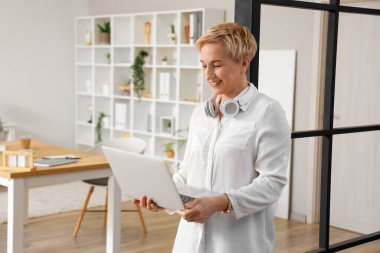 Olgun kadın programcı ofiste dizüstü bilgisayarla çalışıyor.