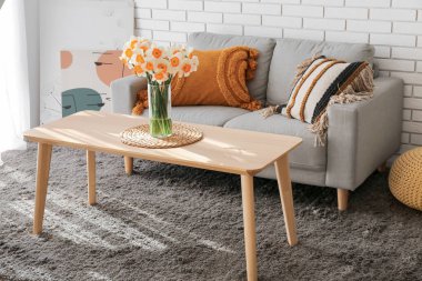 Loş gri kanepe ve çiçek açan narsist çiçeklerle aydınlık oturma odasının içinde.