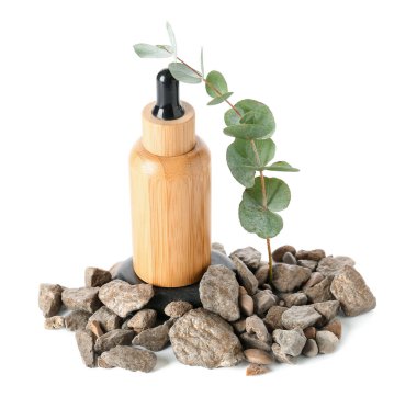 Kozmetik yağlı ahşap şişe, okaliptüs dalı ve beyaz zemin üzerinde taşlar