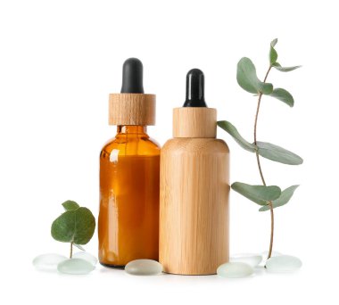 Kozmetik yağlı şişe, okaliptüs dalı ve beyaz arka planda taşlar