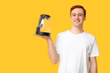 Sarı arka planda modern elektrikli su ısıtıcısı olan yakışıklı genç adam.