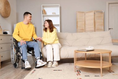 Kız arkadaşı evde el ele tutuşan tekerlekli sandalyedeki genç adam.