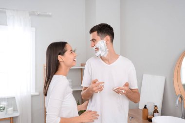 Mutlu genç bir kadın ve kocasının banyoda yüzünde tıraş köpüğü olan bir sabah.