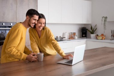 Evde dizüstü bilgisayarı ve bir fincan çayı olan mutlu genç çift.