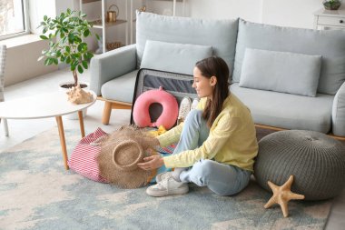 Elinde hasır şapkalı güzel bir kadın oturma odasının içinde bavul hazırlıyor.