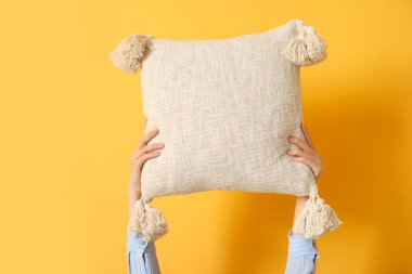 Turuncu arka planda yastığı tutan kadın eller.