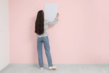 Genç bir kadın odadaki pembe duvara resim çerçevesi asıyor.