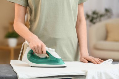 Kadın evde temiz çamaşır ütülüyor.