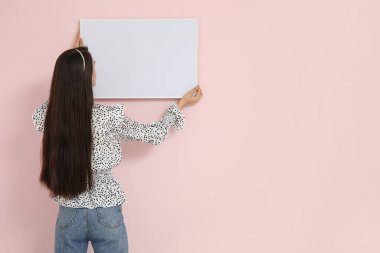 Genç bir kadın odadaki pembe duvara resim çerçevesi asıyor.