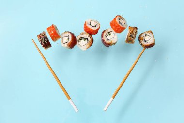 Mavi arka planda lezzetli uçan suşi ruloları ve çubuklar.