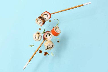 Lezzetli uçan suşi ruloları, soya sosu, salatalık ve yemek çubukları mavi arka planda.